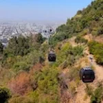 Cabinas del Teleférico Santiago sobre la vegetación del Cerro San Cristóbal, con vistas de la ciudad de Santiago.